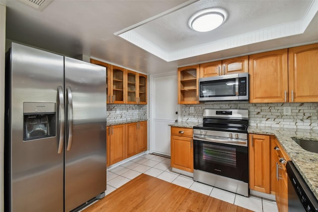 kitchen with decorative backsplash, light stone counters, light tile patterned floors, and appliances with stainless steel finishes