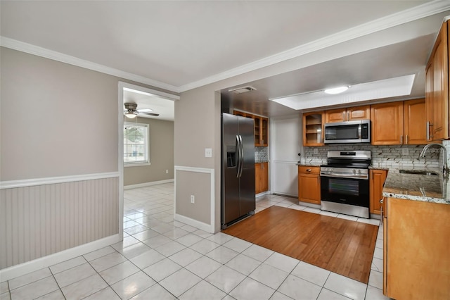 kitchen with sink, light stone counters, backsplash, crown molding, and appliances with stainless steel finishes