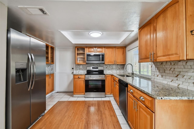 kitchen featuring light stone countertops, appliances with stainless steel finishes, a tray ceiling, sink, and light tile patterned floors