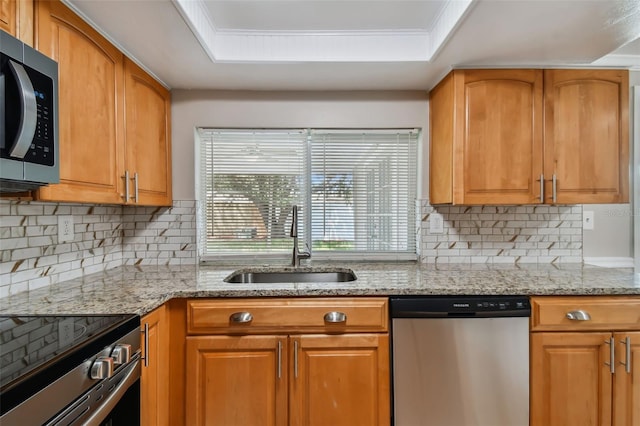 kitchen with decorative backsplash, appliances with stainless steel finishes, light stone counters, a raised ceiling, and sink