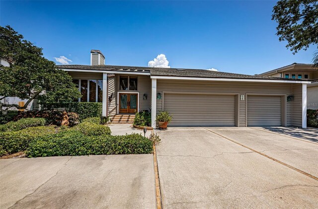 view of front of home featuring concrete driveway, french doors, a chimney, and an attached garage