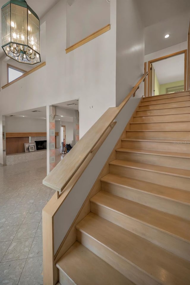 stairway featuring tile patterned flooring, a fireplace, a towering ceiling, and an inviting chandelier