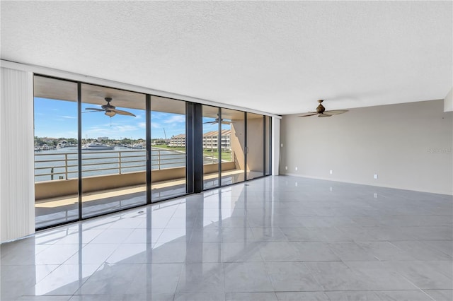 empty room featuring a textured ceiling, expansive windows, a water view, and light tile patterned floors