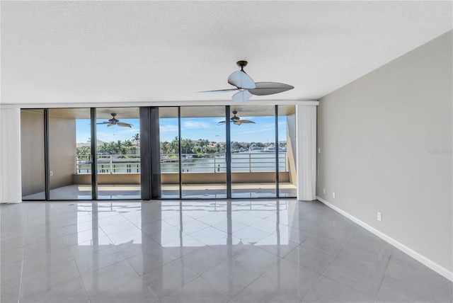 tiled spare room featuring a textured ceiling, a water view, a wall of windows, and ceiling fan