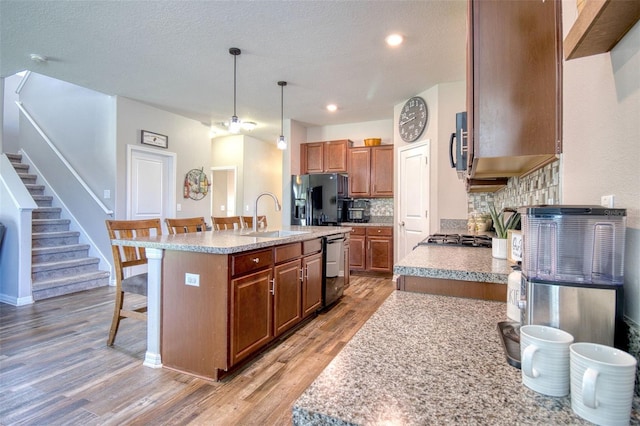 kitchen with a kitchen bar, sink, decorative light fixtures, a kitchen island with sink, and black appliances