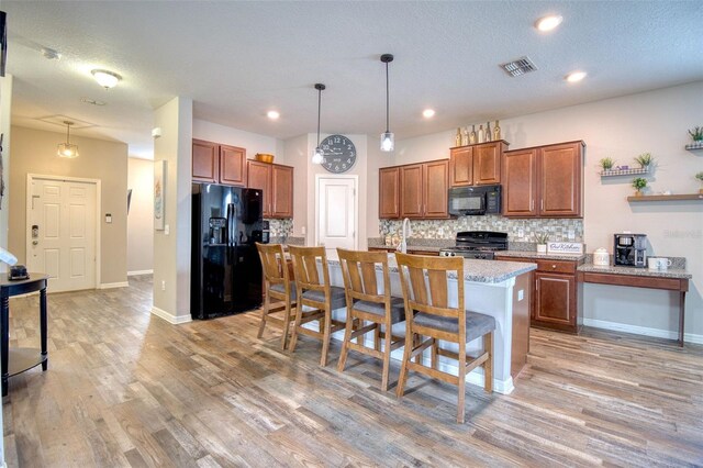 kitchen featuring a kitchen island with sink, hanging light fixtures, black appliances, and a kitchen bar