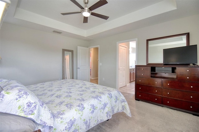 bedroom with a raised ceiling, ceiling fan, light carpet, and ensuite bath