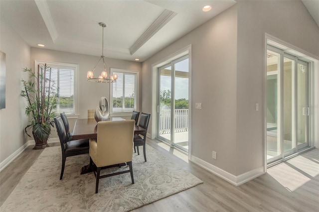 dining room with a raised ceiling, crown molding, an inviting chandelier, and light wood-type flooring