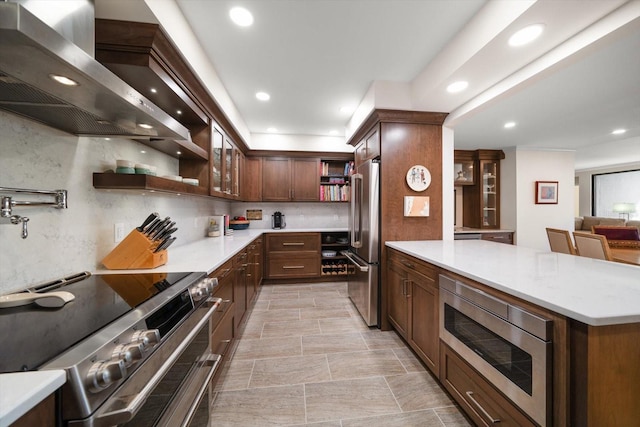 kitchen featuring tasteful backsplash, wall chimney exhaust hood, appliances with stainless steel finishes, light countertops, and open shelves