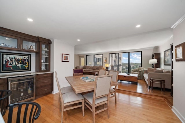 dining room with recessed lighting, beverage cooler, light wood-style floors, a bar, and crown molding