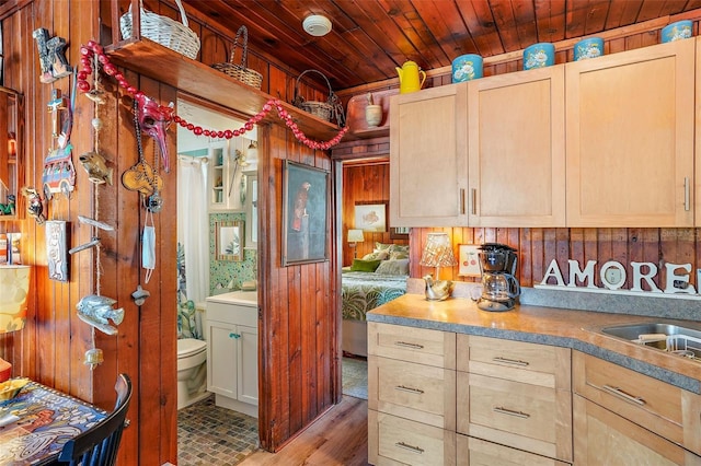 kitchen featuring light brown cabinets, wooden ceiling, sink, and wooden walls