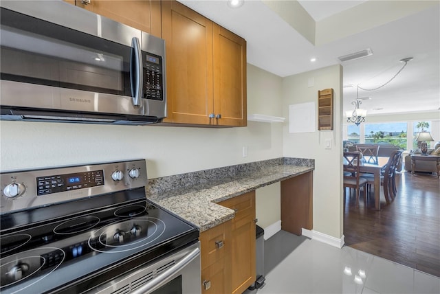 kitchen with light stone countertops, light tile patterned floors, stainless steel appliances, and an inviting chandelier