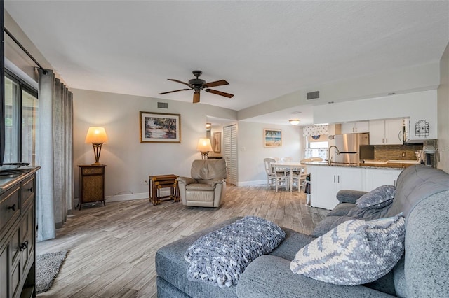 living room featuring ceiling fan, sink, and light hardwood / wood-style floors