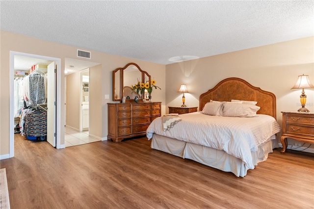 bedroom with ensuite bath, a spacious closet, wood-type flooring, and a textured ceiling