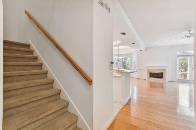 stairs featuring ceiling fan with notable chandelier, sink, wood-type flooring, and a healthy amount of sunlight