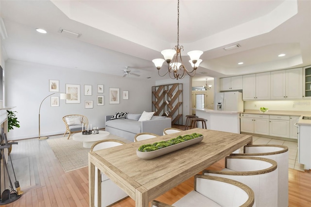 dining space featuring ceiling fan with notable chandelier, light wood-type flooring, and a raised ceiling