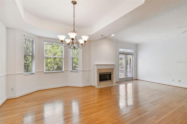 unfurnished living room with a raised ceiling, light wood-type flooring, plenty of natural light, and a chandelier