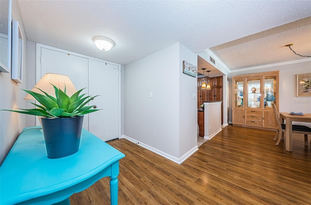 corridor featuring a textured ceiling, crown molding, and dark wood-type flooring