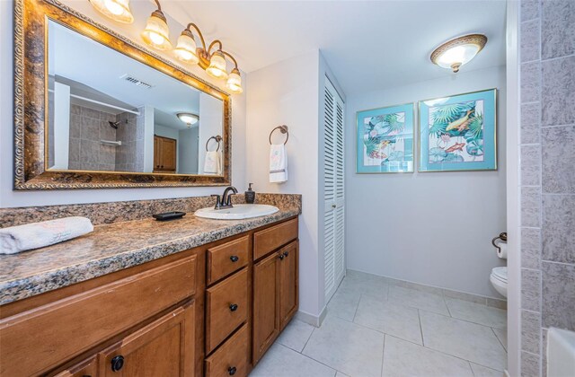 bathroom with tile patterned floors, vanity, a tile shower, and toilet