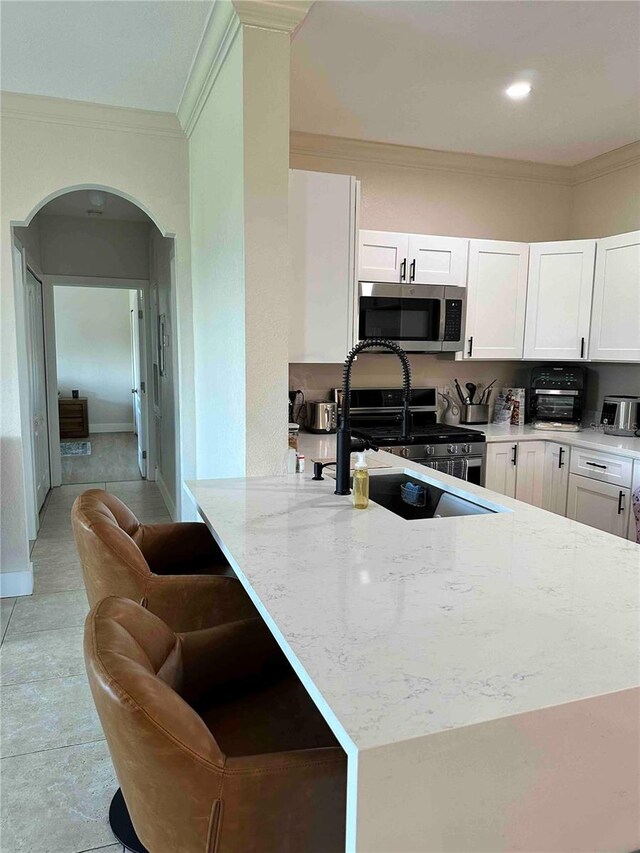 kitchen with crown molding, stainless steel appliances, white cabinetry, light stone countertops, and light tile patterned floors