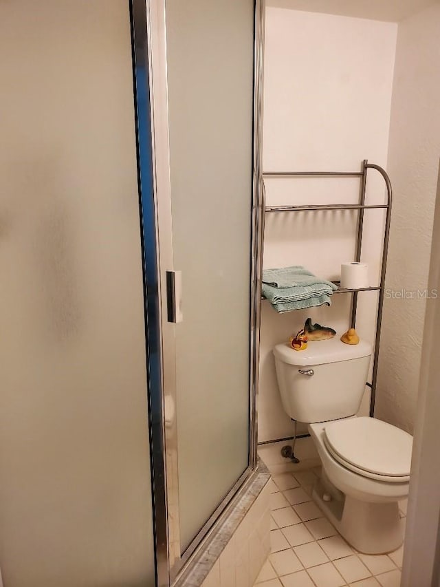 bathroom featuring tile patterned flooring, toilet, and a shower with shower door