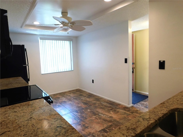 kitchen with a tray ceiling, ceiling fan, black appliances, and light stone counters