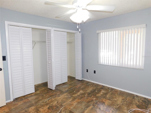 unfurnished bedroom with a textured ceiling, ceiling fan, and multiple closets