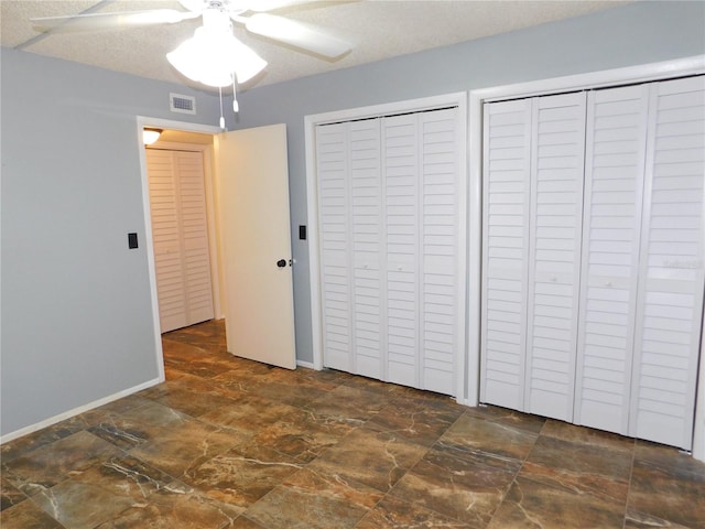 unfurnished bedroom with ceiling fan, a textured ceiling, and two closets