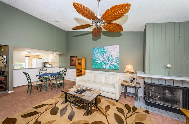 living room with ceiling fan, a textured ceiling, light carpet, and a tiled fireplace