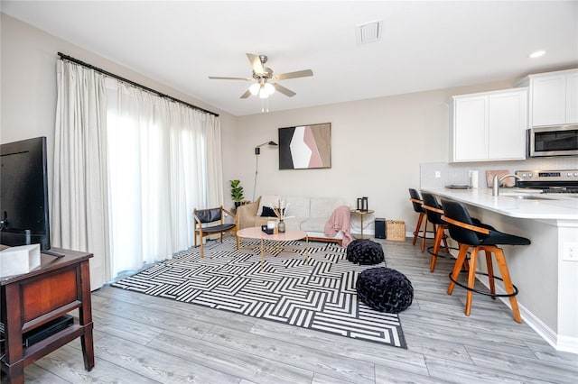 living room with light hardwood / wood-style flooring, ceiling fan, and sink