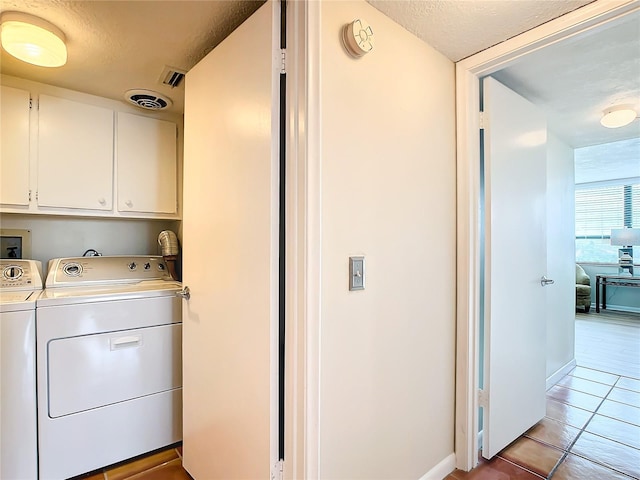 washroom with cabinets, light tile patterned floors, a textured ceiling, and washing machine and clothes dryer