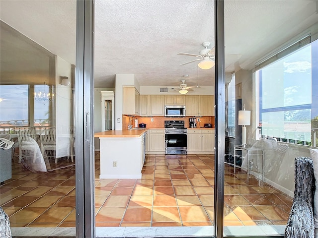 kitchen featuring light brown cabinetry, light tile patterned floors, stainless steel appliances, and a textured ceiling