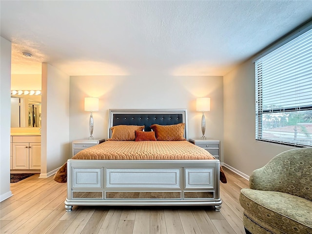 bedroom with connected bathroom, light hardwood / wood-style floors, and a textured ceiling