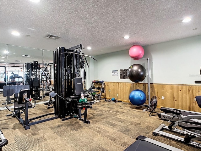 workout area featuring light carpet, a textured ceiling, and wood walls