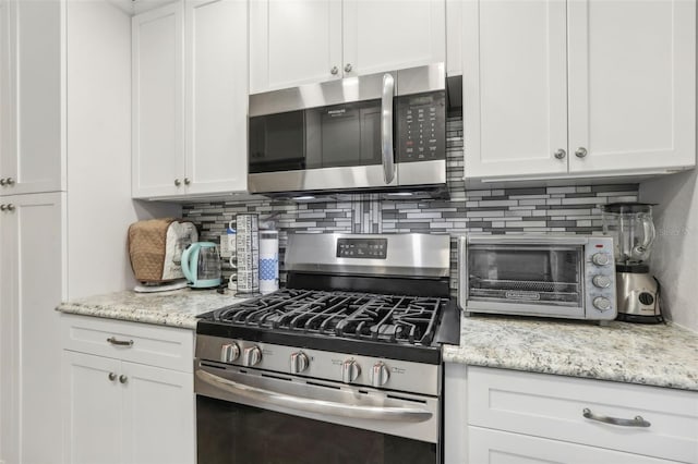 kitchen with white cabinets, appliances with stainless steel finishes, tasteful backsplash, and light stone countertops