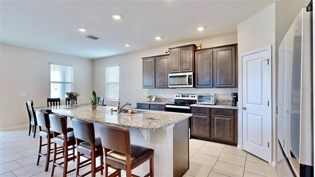 kitchen with a center island with sink, dark brown cabinetry, light tile floors, sink, and appliances with stainless steel finishes