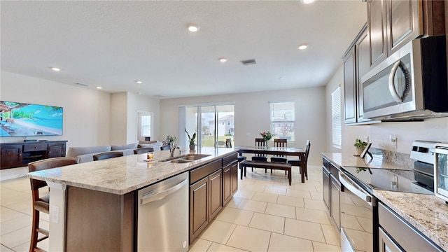 kitchen with a center island with sink, light tile flooring, light stone counters, sink, and appliances with stainless steel finishes