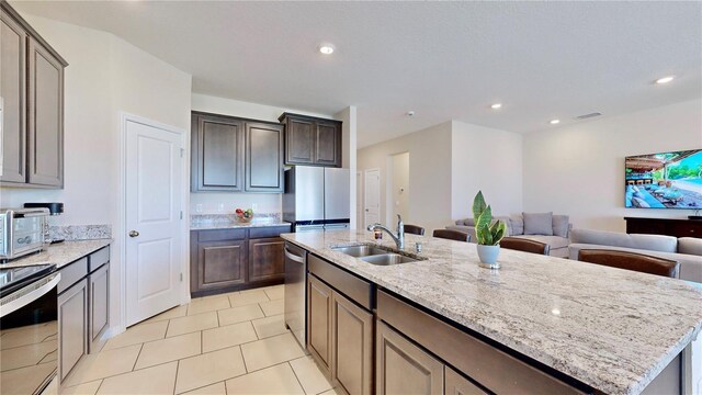 kitchen featuring light stone countertops, light tile floors, sink, a kitchen island with sink, and appliances with stainless steel finishes