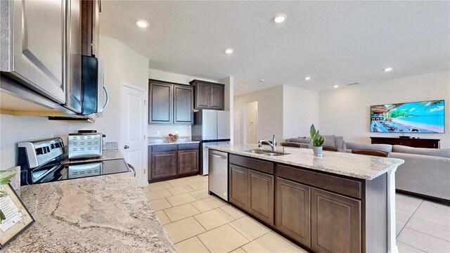 kitchen featuring light stone counters, light tile flooring, dishwasher, stove, and an island with sink