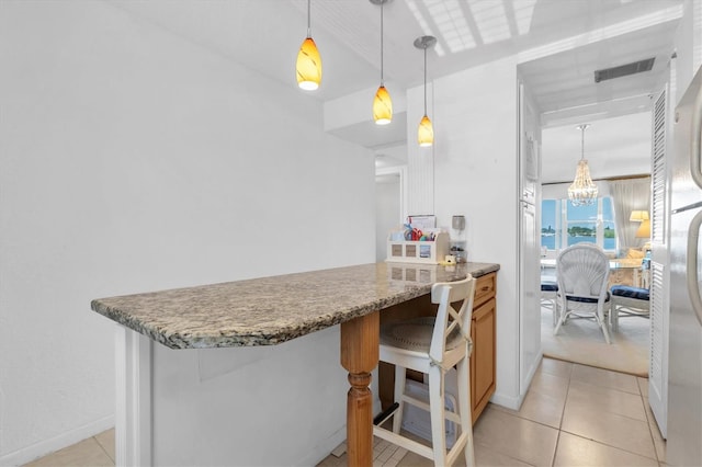 kitchen with a notable chandelier, a breakfast bar area, stone countertops, and pendant lighting