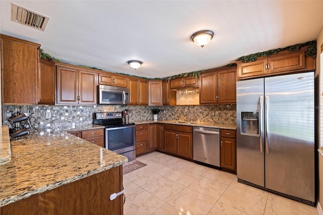 kitchen featuring light tile patterned floors, backsplash, light stone counters, and stainless steel appliances