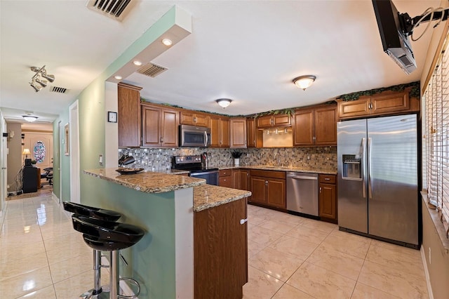 kitchen featuring light stone counters, a breakfast bar, brown cabinets, visible vents, and appliances with stainless steel finishes