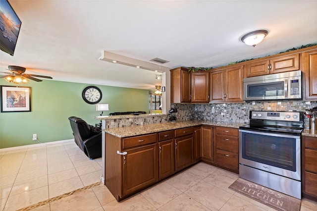 kitchen with light stone countertops, stainless steel appliances, a peninsula, a ceiling fan, and decorative backsplash