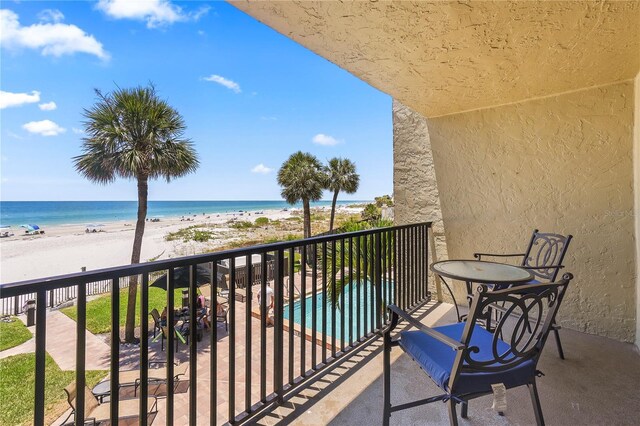 balcony featuring a water view, a view of the beach, and a fenced in pool