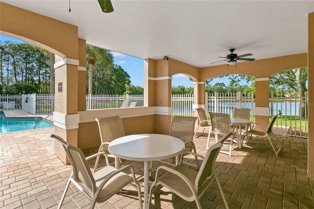 view of patio with ceiling fan, a water view, and a fenced in pool