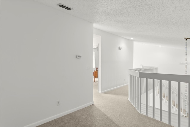 corridor featuring light carpet, visible vents, baseboards, and a textured ceiling