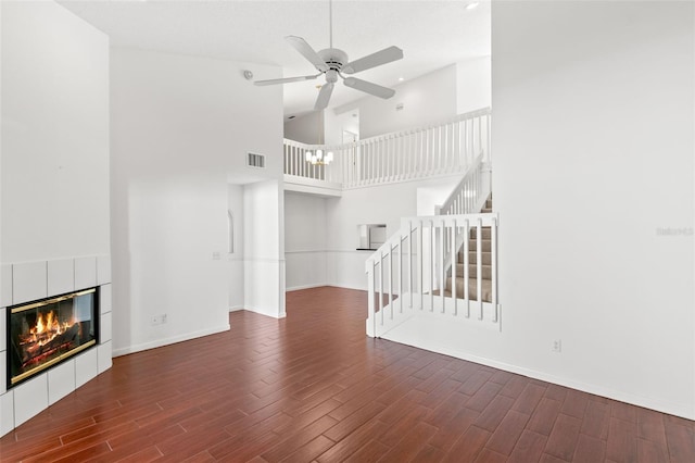 unfurnished living room featuring ceiling fan, baseboards, stairway, a tiled fireplace, and dark wood finished floors