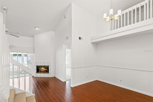 unfurnished living room with visible vents, dark wood finished floors, a tile fireplace, a wainscoted wall, and ceiling fan with notable chandelier