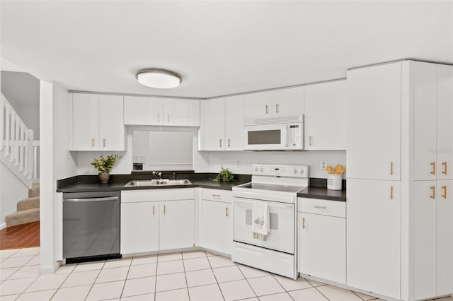 kitchen with dark countertops, white cabinetry, a sink, light tile patterned flooring, and white appliances