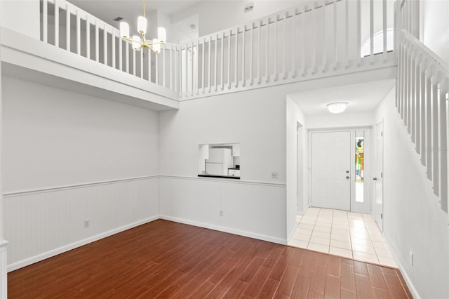 entrance foyer with a notable chandelier, a wainscoted wall, wood finished floors, a towering ceiling, and stairway